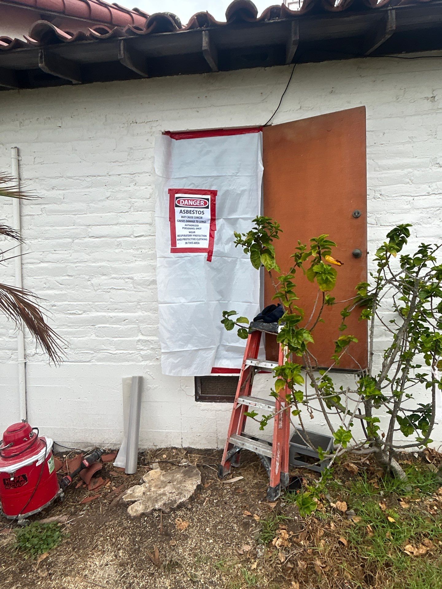 Asbestos warning sign and plastic containment at a VenTERRA project entrance in Pismo Beach
